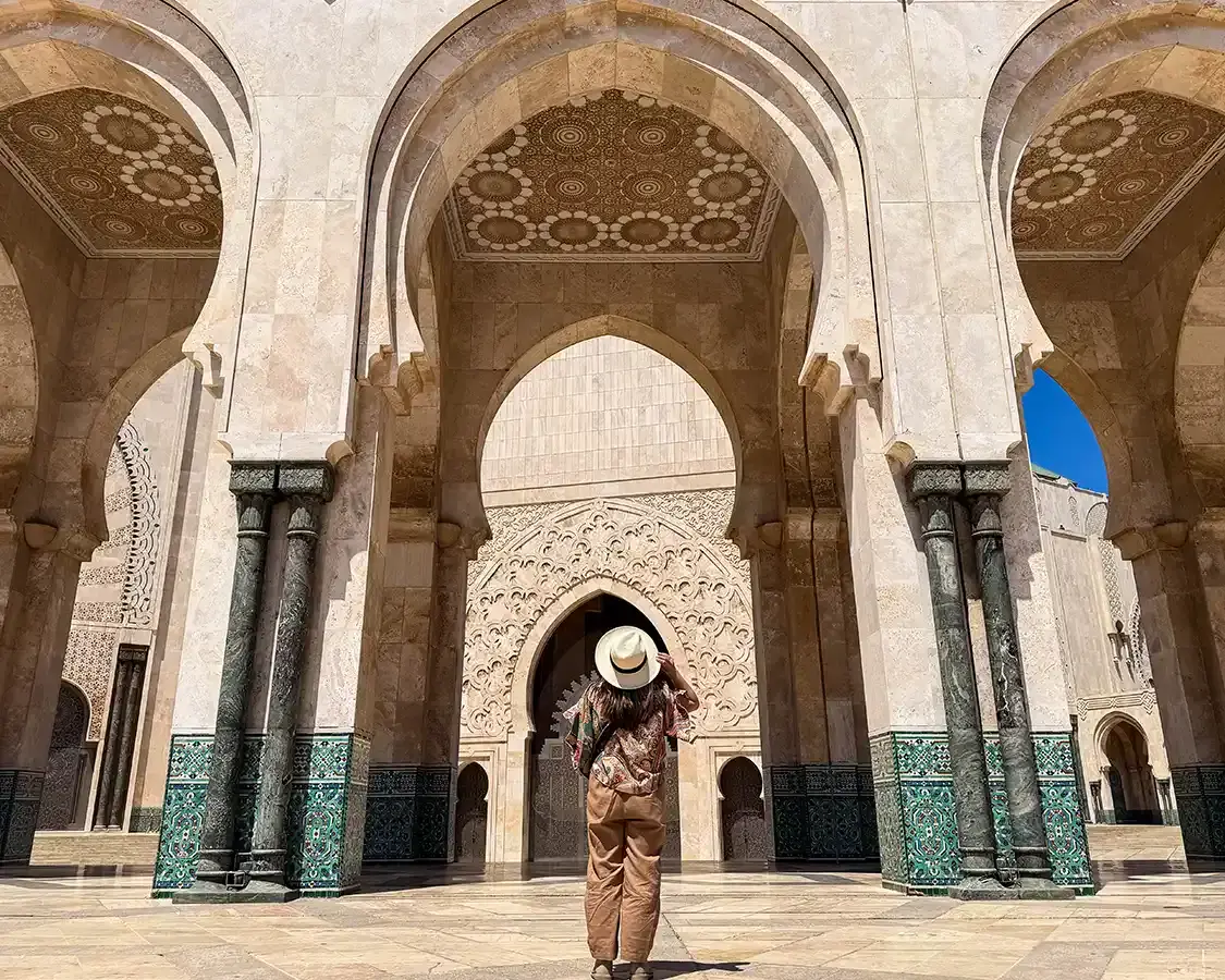 A woman holds her hat while looking up at the Hassan II Mosque in Casablanca Morocco