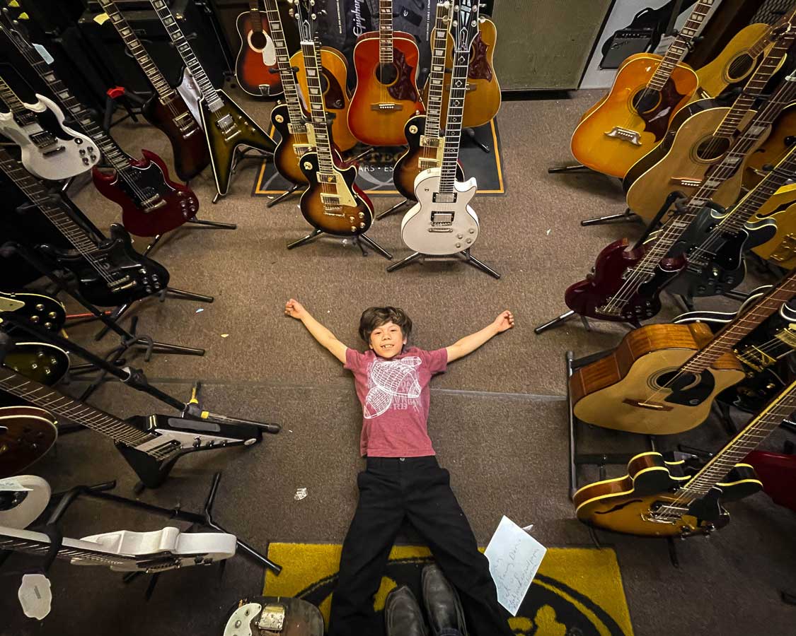 Boy surrounded by instruments at Rochester House of Guitars