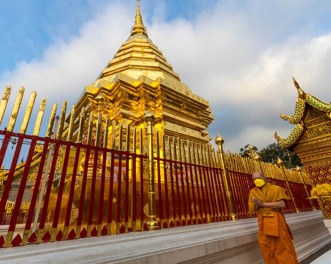 A Buddhist monk walks past a golden temple in Chiang Mai, Thailand