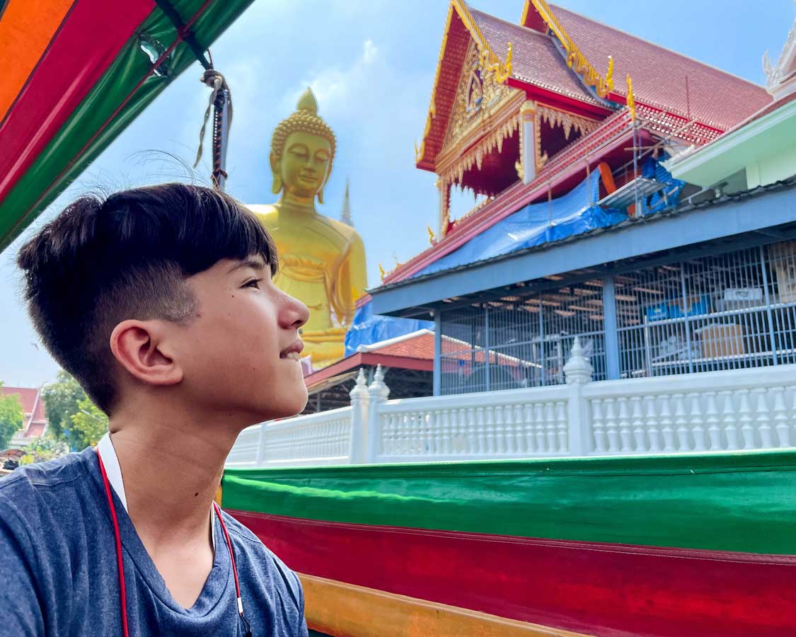 A boy looks at a tall Buddha Statue at Royal Wat Paknam Phasi Charoen temple in Bangkok, Thailand