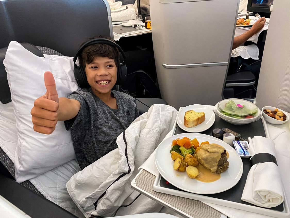 Boy flying in business class giving thumbs up with a plate of food in front of him