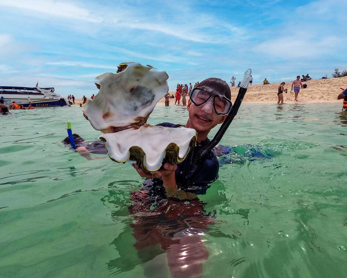 Boy shows off a giant clam near Krabi, Thailand with kids