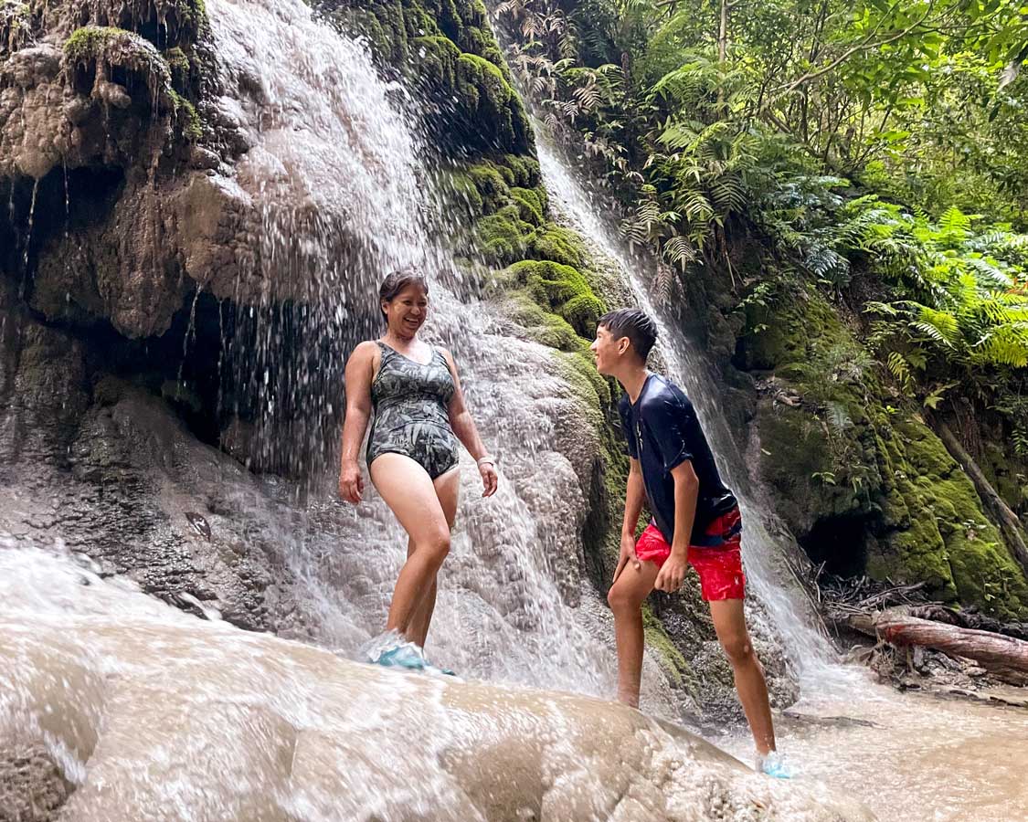 Mother and son laughing under a waterfall in Thailand