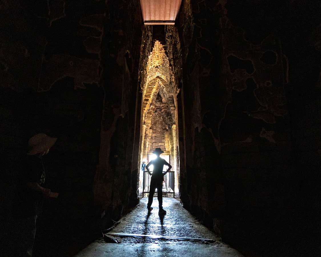 Boy silhouetted with his hands on his hips against the entrance of Wat Ratchaburana in Ayutthaya