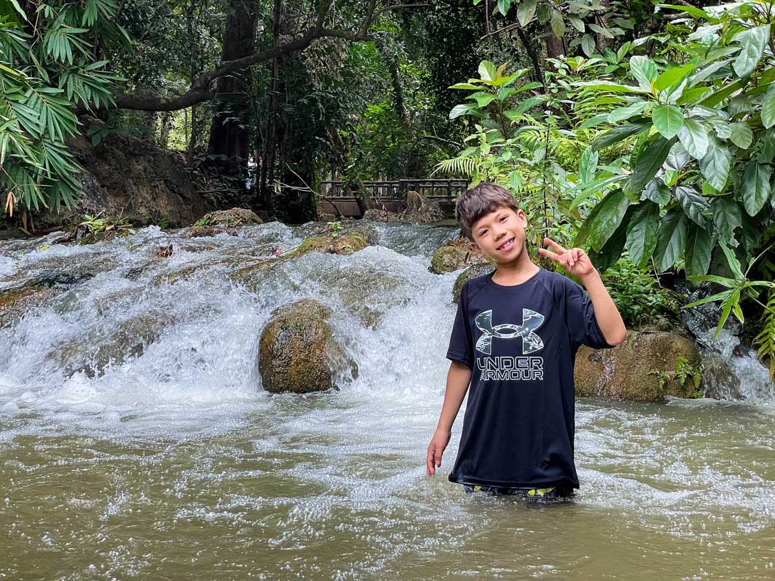 Young boy wades in the waters of Sai Yok Waterfall