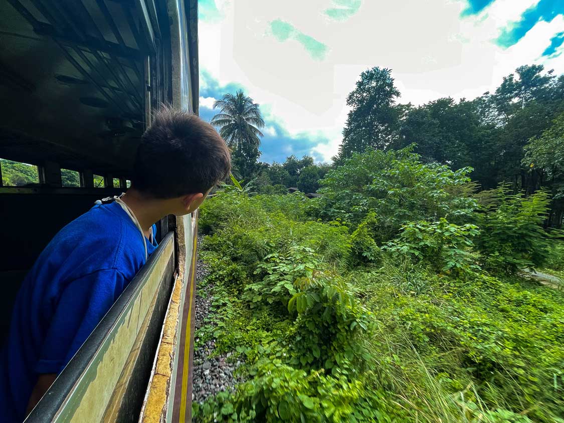 Boy sticks his head out of the window of the Death Railroad train in Kanchanaburi, Thailand