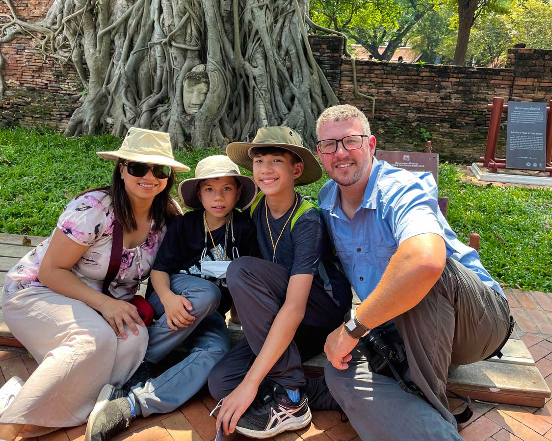 Wandering Wagars family sitting in front of a Buddha statue that is covered in tree roots