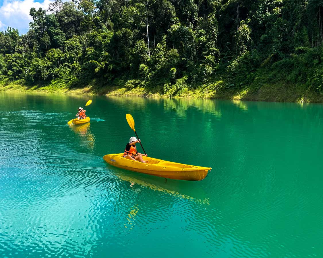 A boy and his mom paddle yellow kayaks on blue waters at Khao Sok National Park