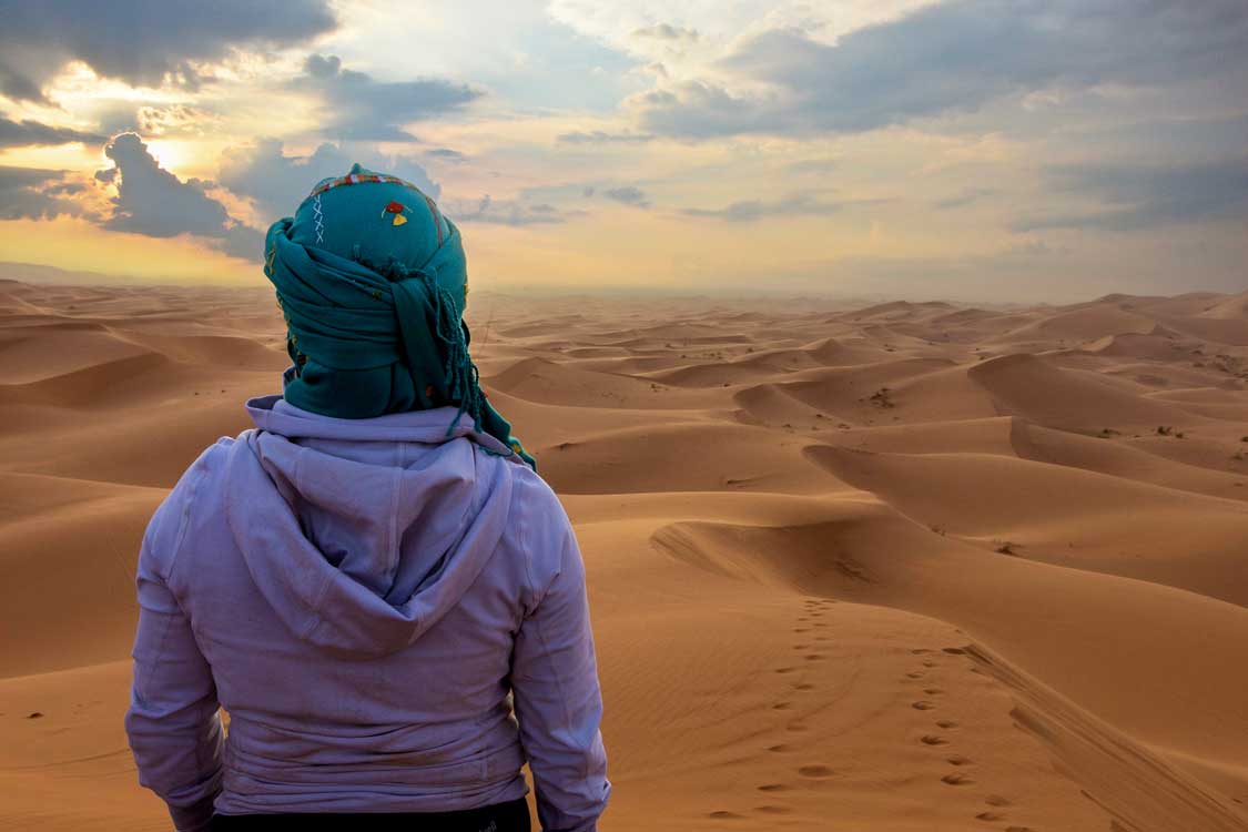 A woman looks out over the sand dunes of the Sahara Desert from the Berber glamping camps near Merzouga, Morocco