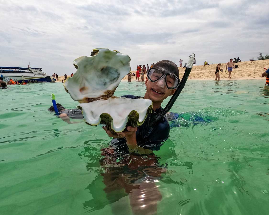 A boy holds up a giant clam at a beach in Phuket