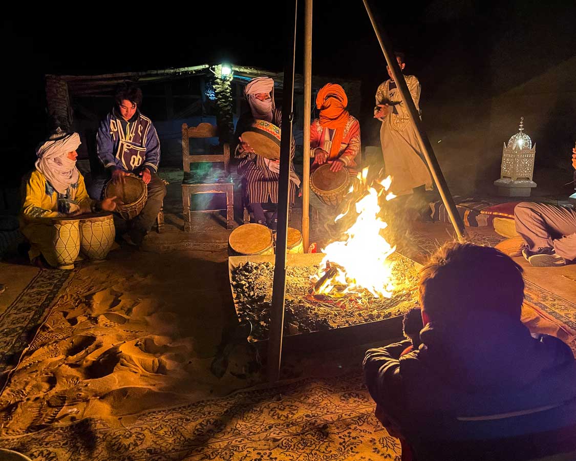 A boy watches a group of Berber musician in front of a campfire in Merzouga, Morocco