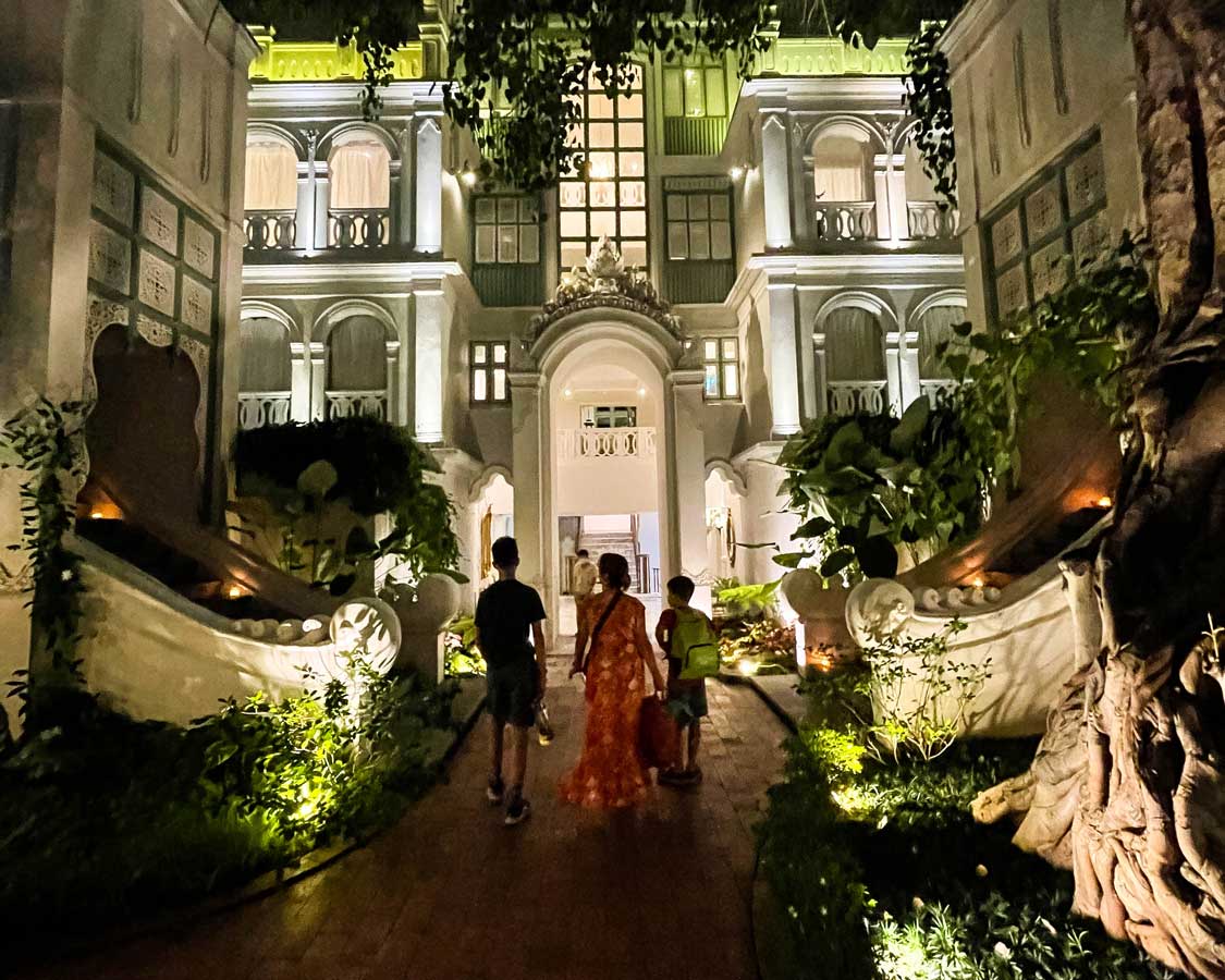 A woman and two children walk through a scenic courtyard at The Inside House at night