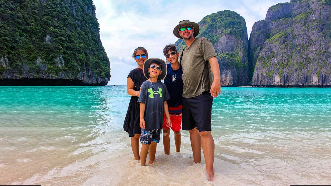 How to stay healthy while traveling - a mixed race family smiles at the camera from blue waters in a Thailand lagoon