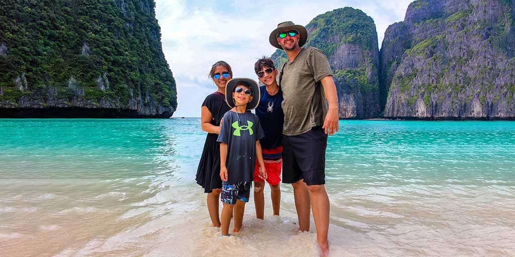 How to stay healthy while traveling - a mixed race family smiles at the camera from blue waters in a Thailand lagoon