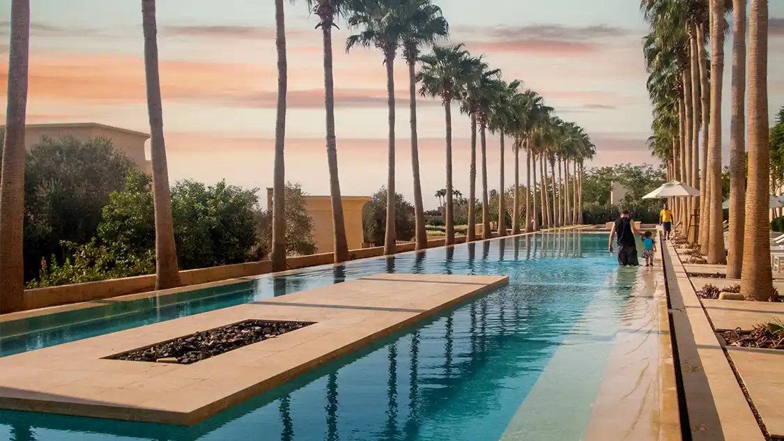 A father walks with his on through a palm-lined pool at the Kempinski Hotel Ishtar Dead Sea in Jordan