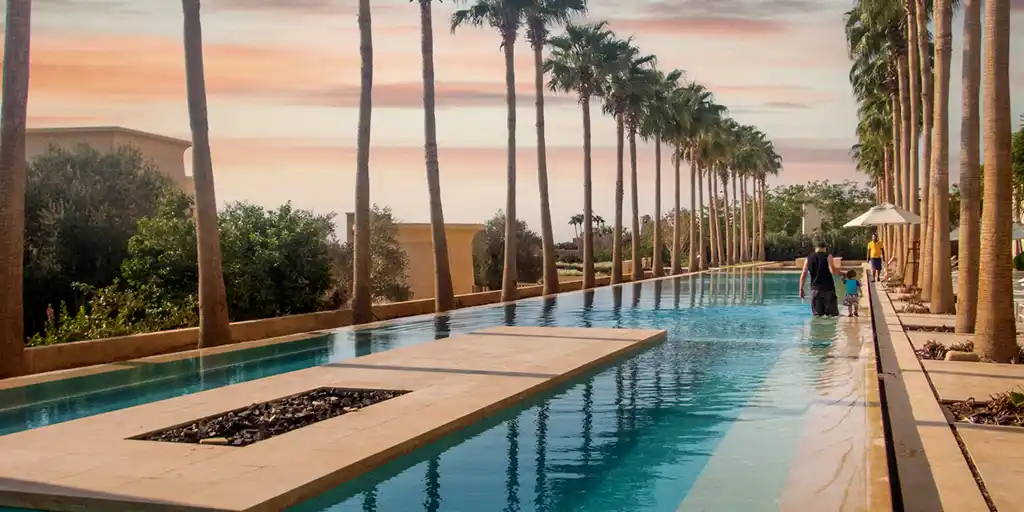 A father walks with his on through a palm-lined pool at the Kempinski Hotel Ishtar Dead Sea in Jordan