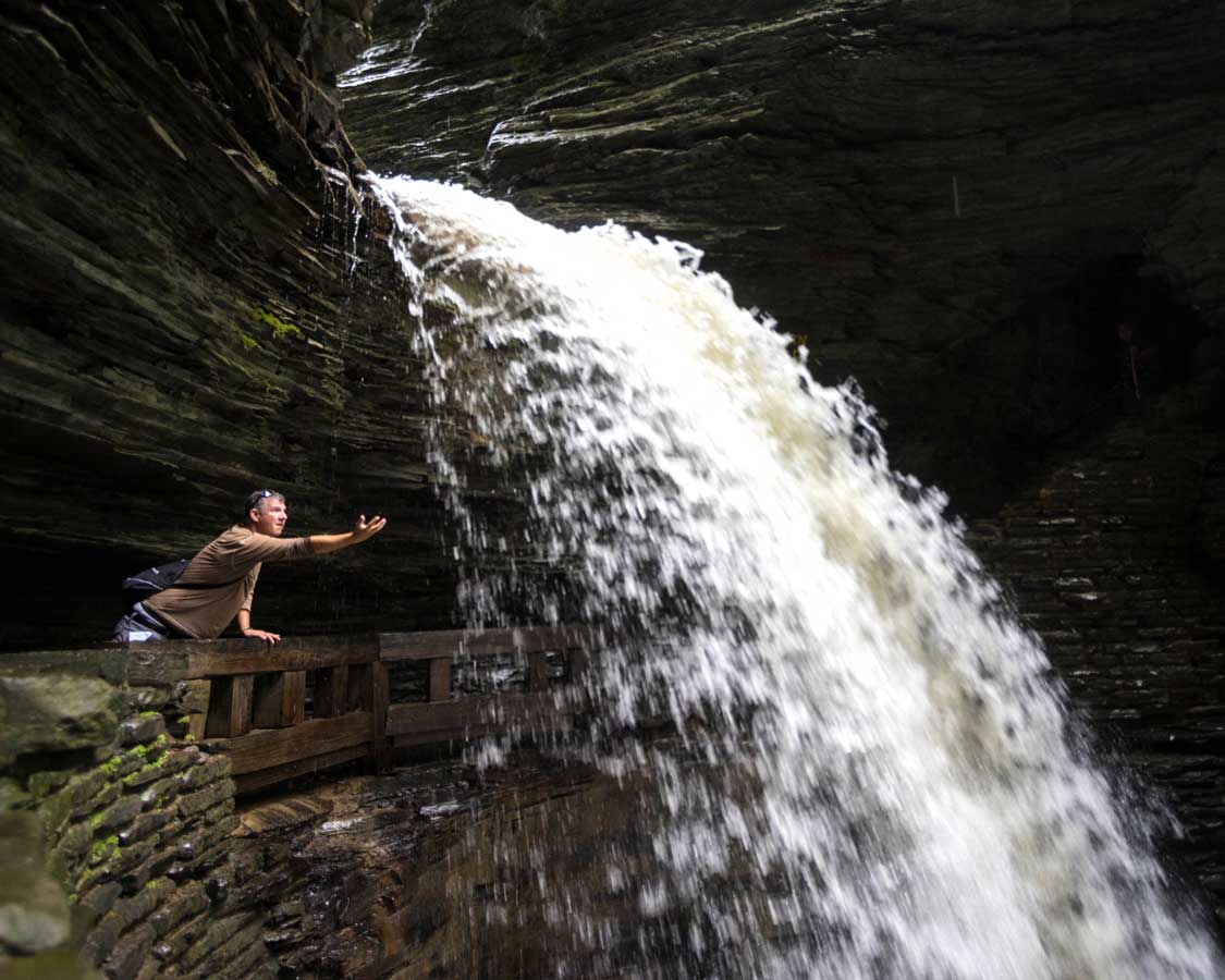 A man hiking Watkins Glen State Park reaches out to touch a waterfall