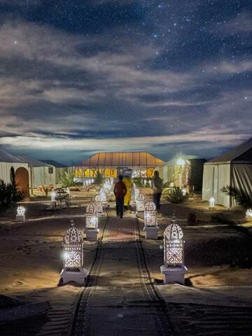 A boy walks down a walkway under starry skies at a Merzouga Luxury Desert Camp