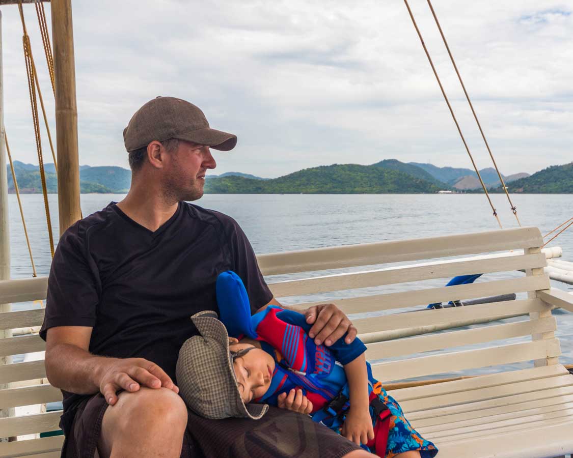 Father sits with his sleeping son on a boat in the Philippines