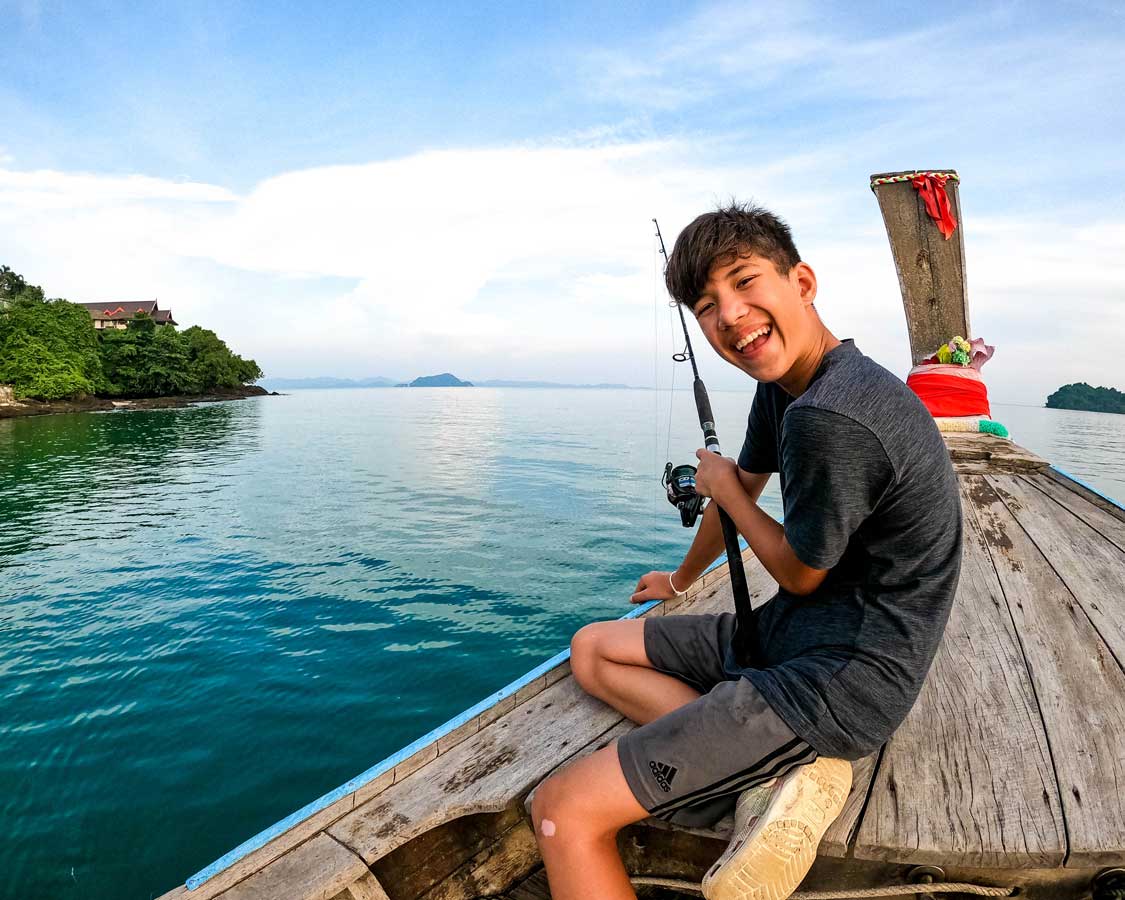 A smiling boy fishing from a longtail boat in Phuket