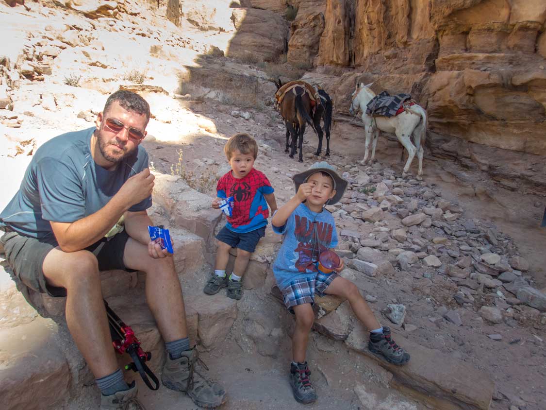 A father and his two young  sons stop for a snack while hiking to the Petra Monastery in Jordan