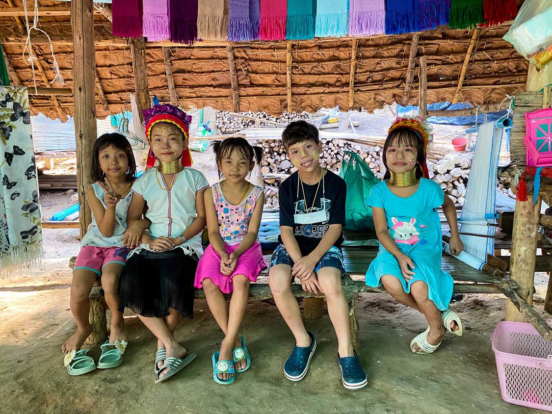 A western boy sits with smiling children from a Karen village in Northern Thailand