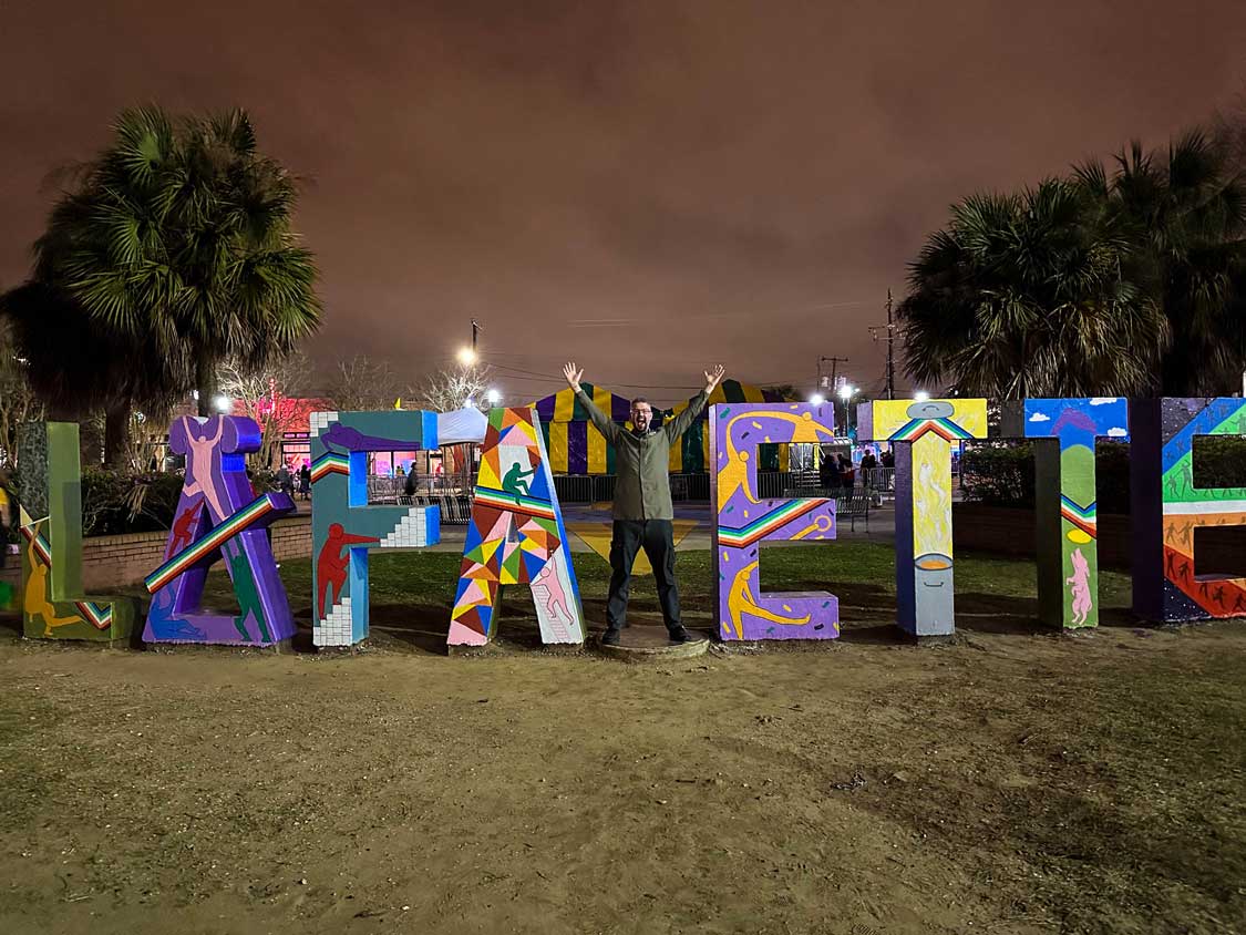 A may raises his arms in a "Y" between the colourful letters of "Lafayette"
