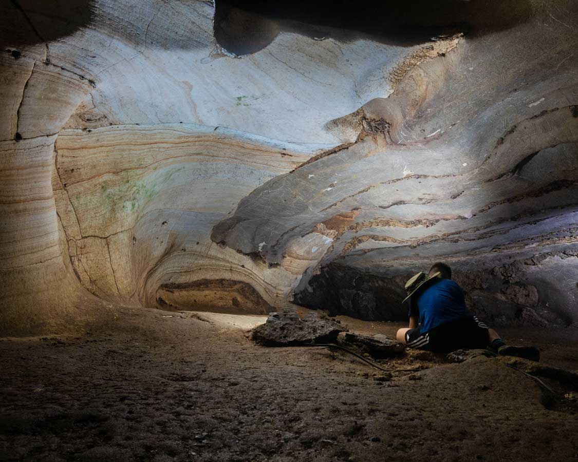A boy kneelse down in a scenic lit cave in Sai Yok National Park, Thailand