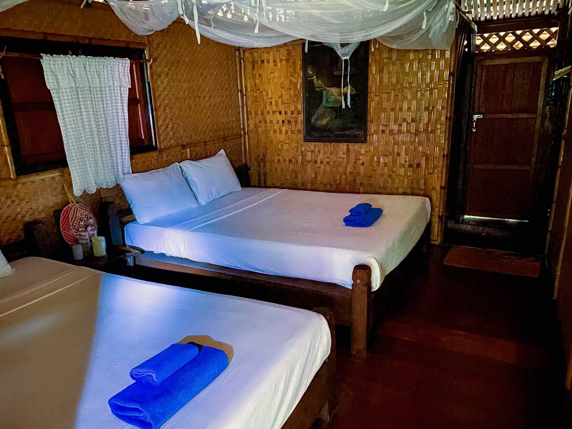 A sparsely decorated room with teak and bamboo trim with two beds with blue towels