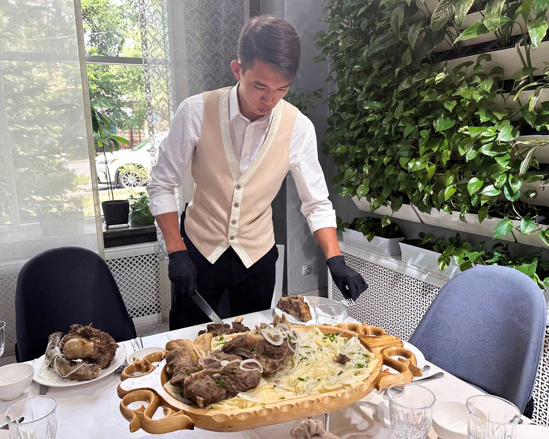 A waiter carves meat for a dish of beshparmak made with noodles and onions