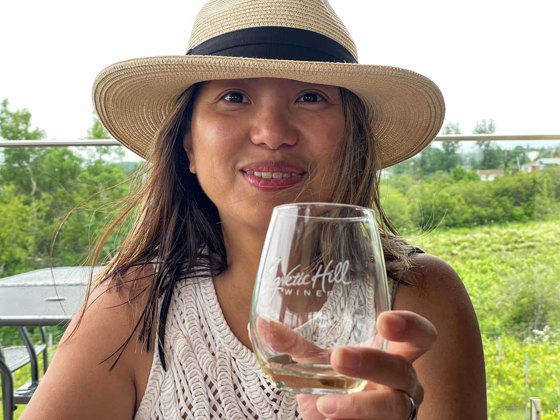 A woman wearing a fedora sips wine at a vineyard in Magnetic Hill Winery