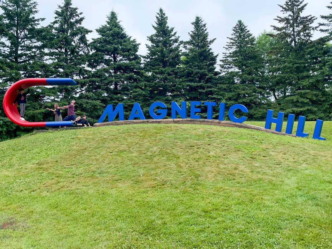 A family playing on a large sign for Magnetic Hill Canada