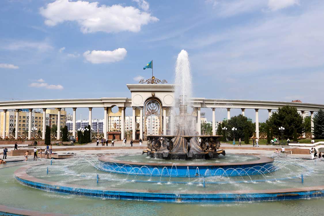 Children play in a large fountain in front of an arched monument at First President's Park in central Almaty