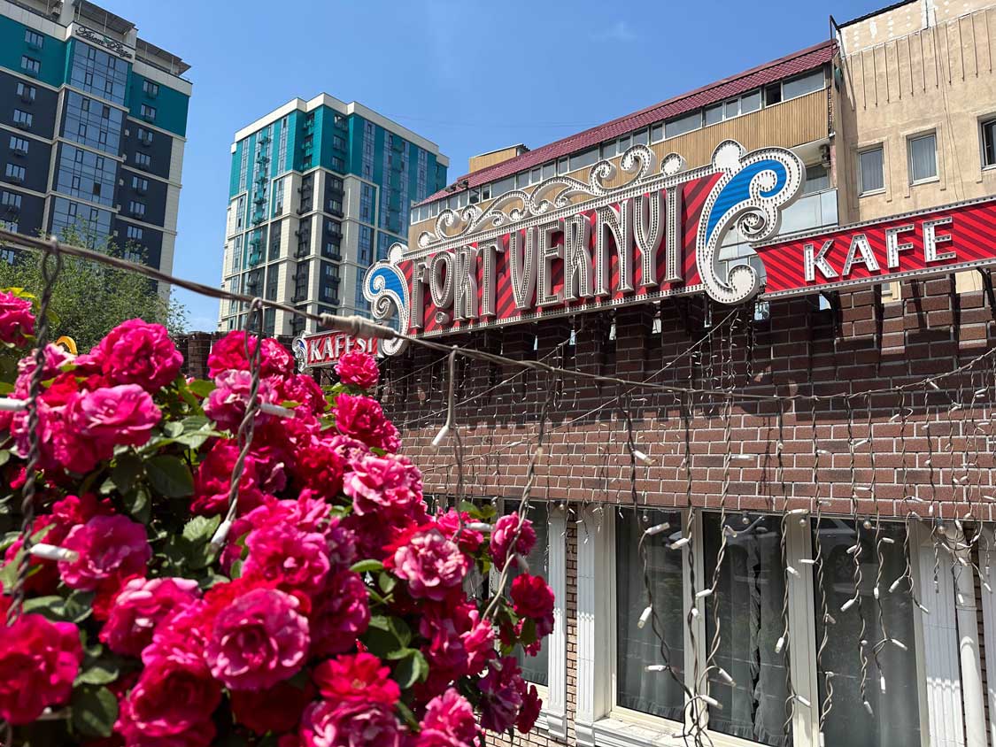 A restaurant facade with a sign saying "Fort Verny" behind a red rose bush