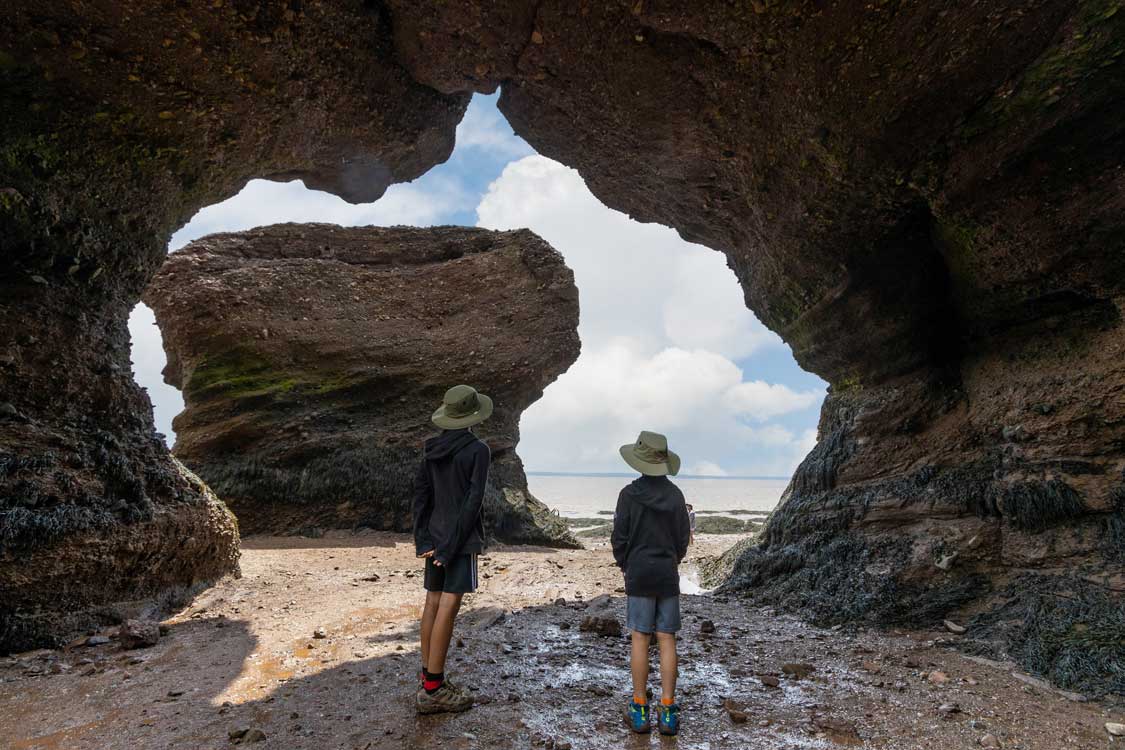 Children stand in a rock arch at Hopewell Rocks, New Brunswick