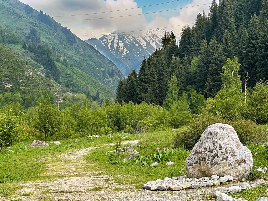 A rock with animal petroglyphs sits at the entrance of a trail through the mountains of Ile-Atalau National Park in Almaty