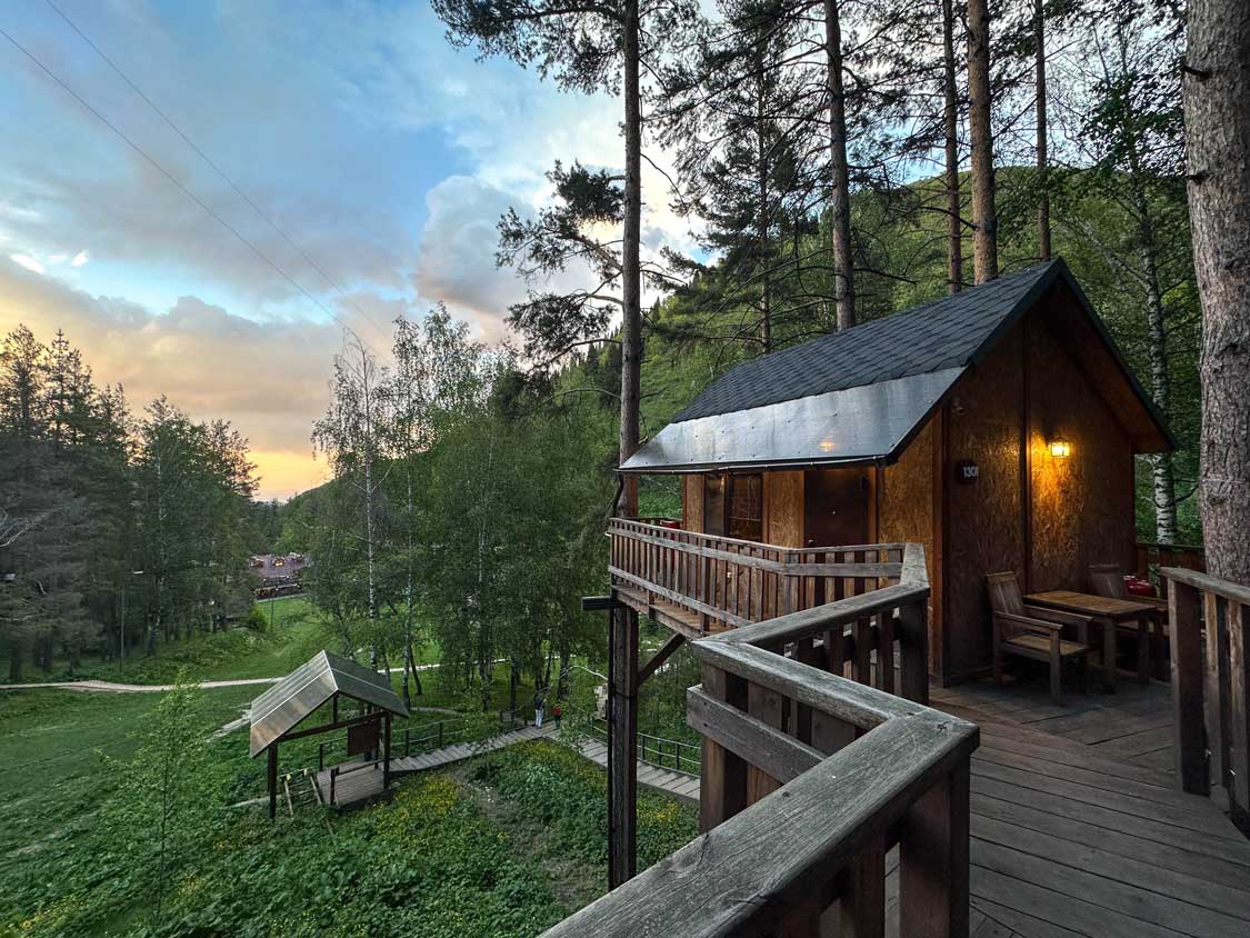 A boardwalk leading to a treetop village with a sunset in the background at Oi-Qaragai mountain resort in Kazakhstan