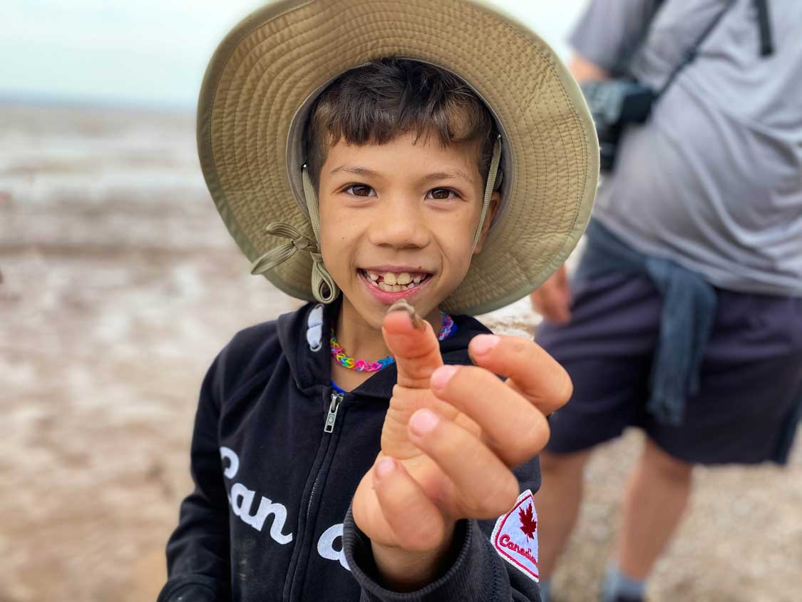 A young boy holds up a tiny Corophium volutator shrimp at Hopewell Rocks beach