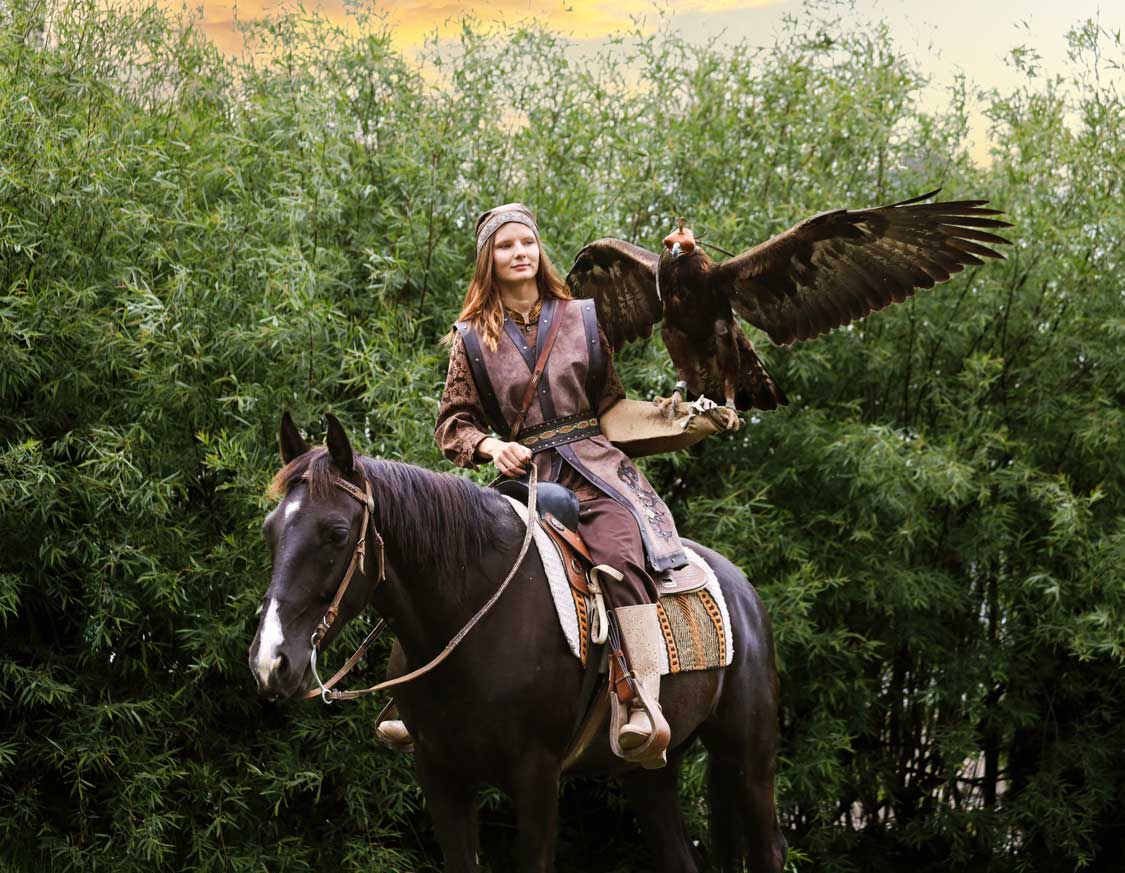 A nomadic woman on horseback holds a hunting eagle with its wings outspread at the Sunkar Bird Refuge in Almaty