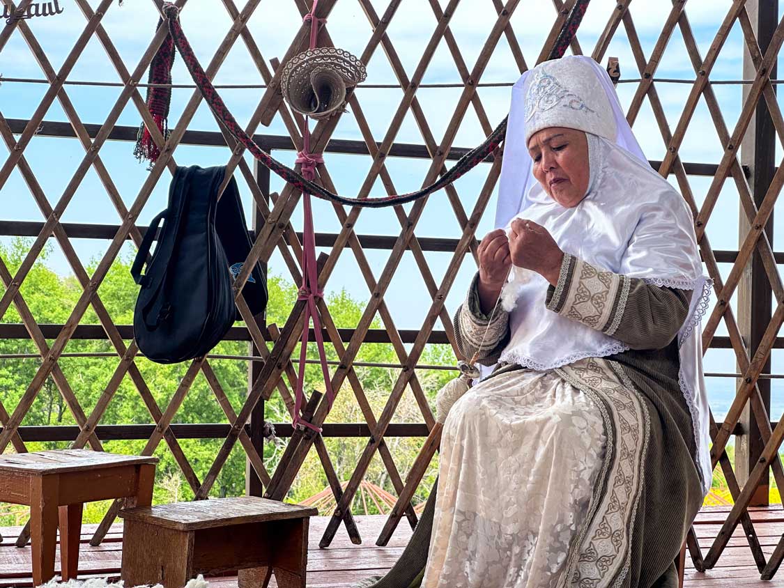 A woman in traditional nomadic garb knits using fresh wool in a yurt