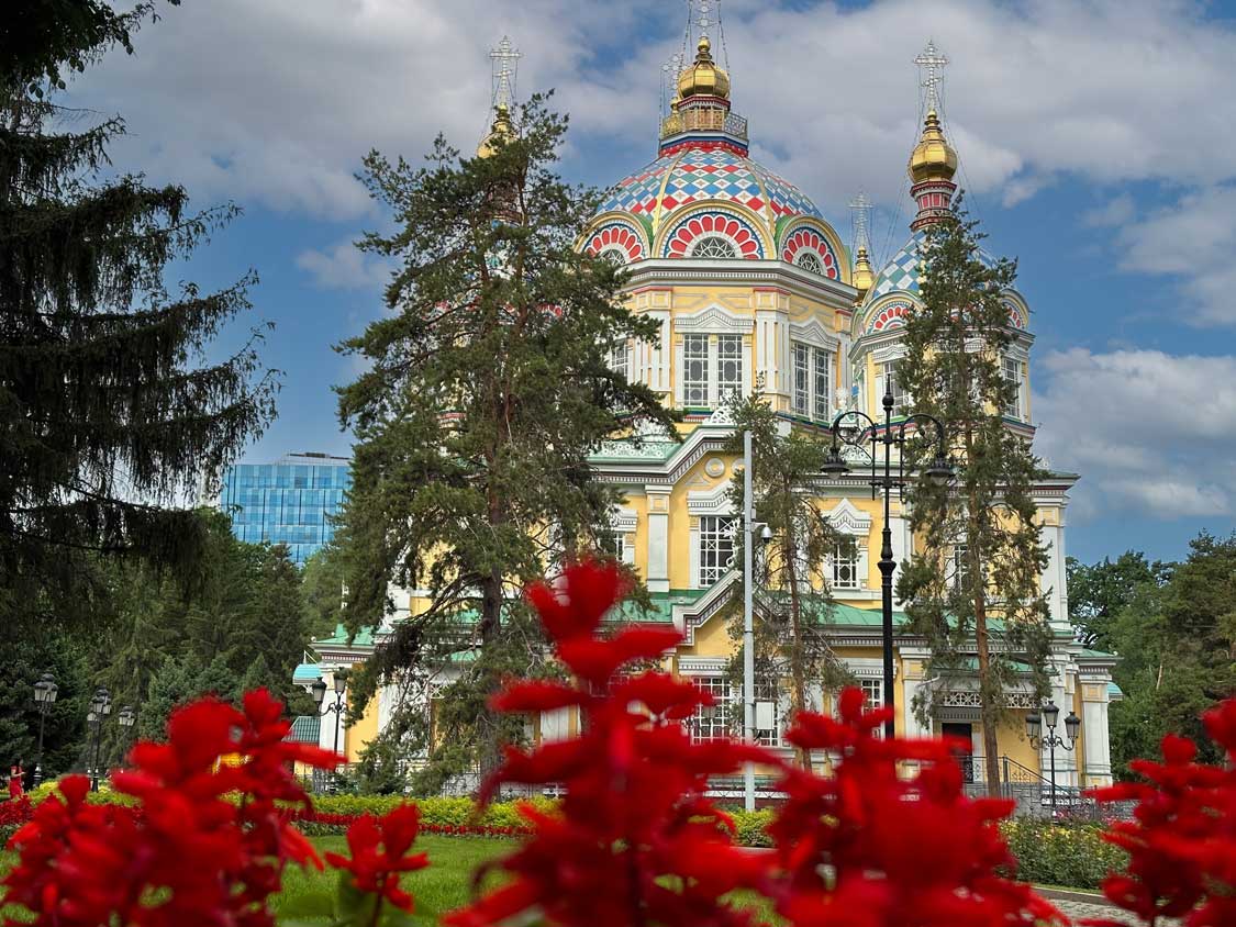 A colorful wood cathedral behind trees and red flowers