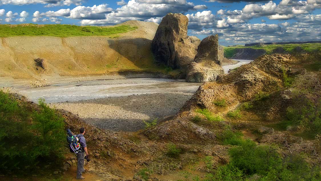 A man stands on a riverbed staring at the rock formations of Hijodaklettar Iceland