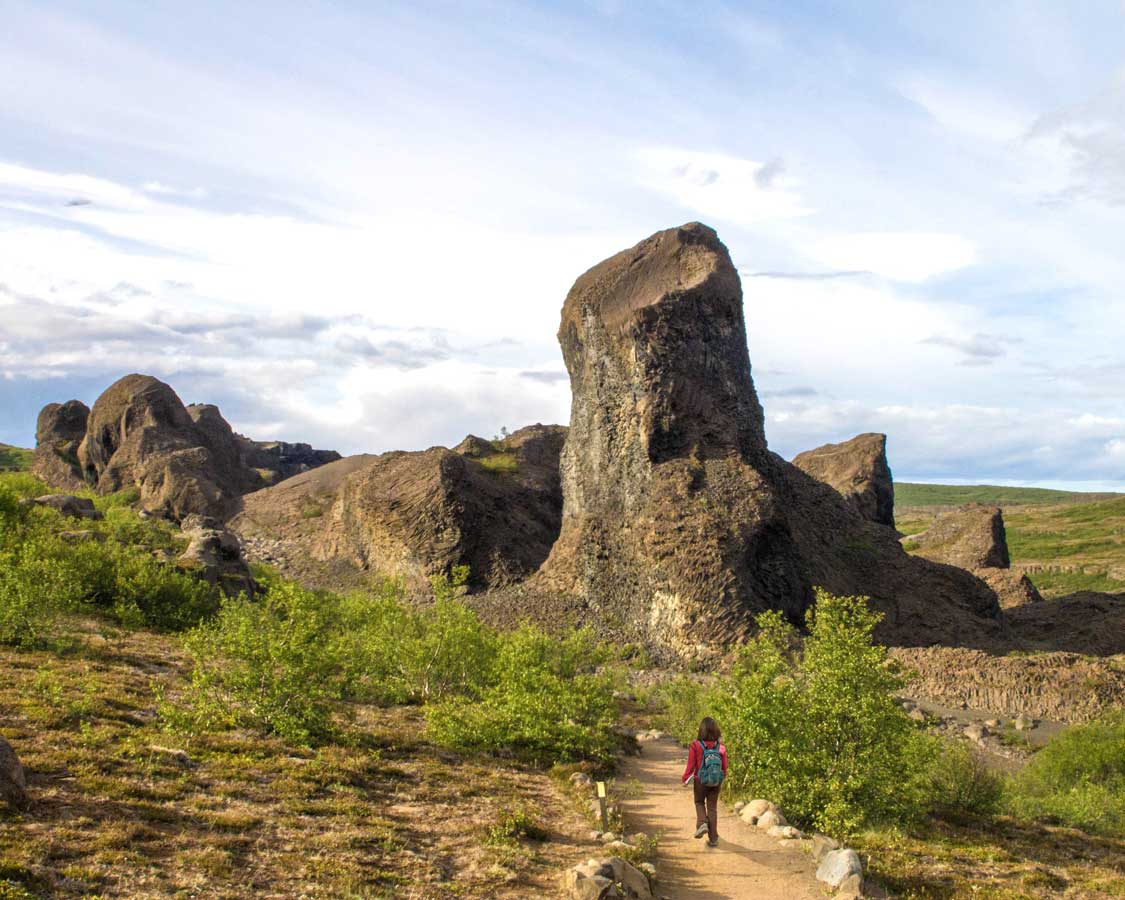 A woman walks along a hiking trail to a tall rock formation called the Troll