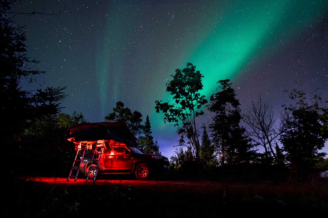 green Northern lights above a campground with a truck with a rooftop tent