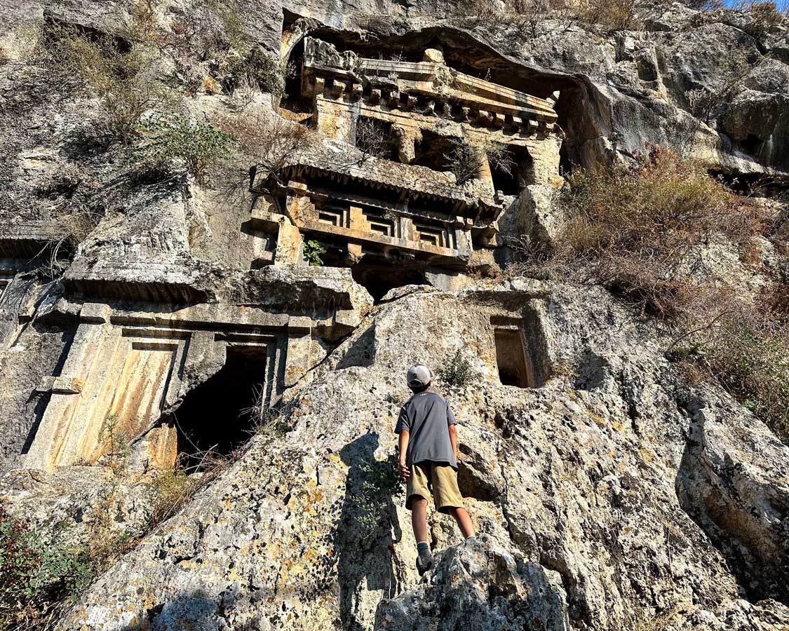 A boy scales a rock to see the Lycian Rock Tombs in Fethiye, Turky