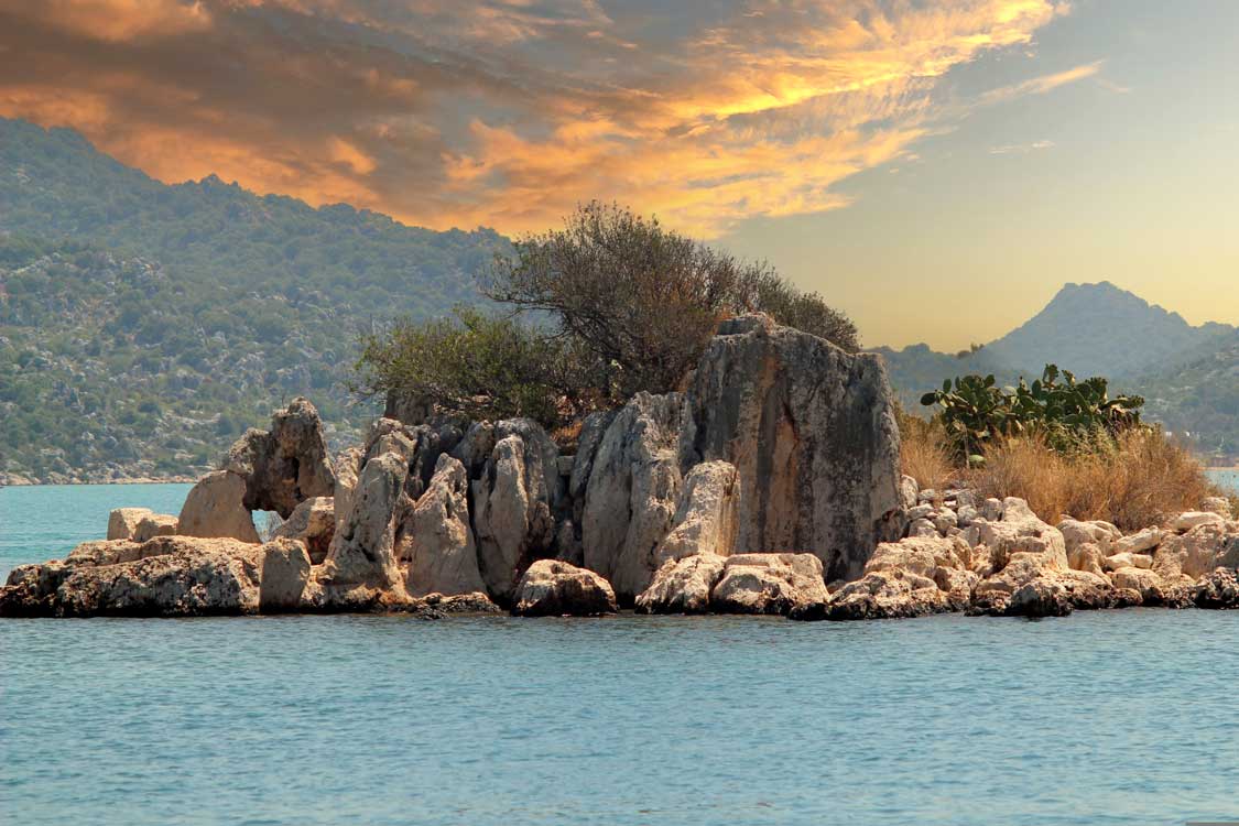 Ancient ruins on an island near Olympos, Turkiye lit by a beautiful sunset