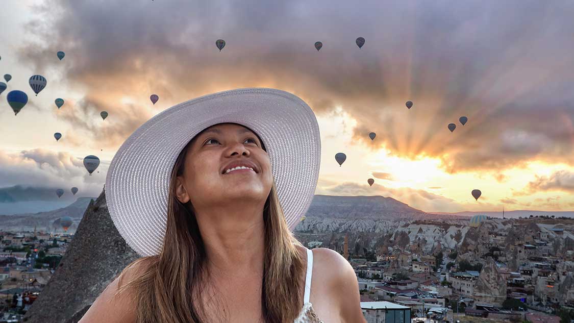 Turkiye family travel blog - woman standing in front of a sunrise in Cappadocia, Turkiye with hot air balloons filling the sky