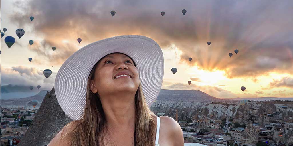 Turkiye family travel blog - woman standing in front of a sunrise in Cappadocia, Turkiye with hot air balloons filling the sky