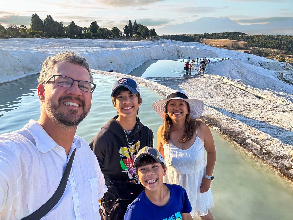 Wandering Wagars family smiling in front of the geothermal pools at Pummakale, Turkiye