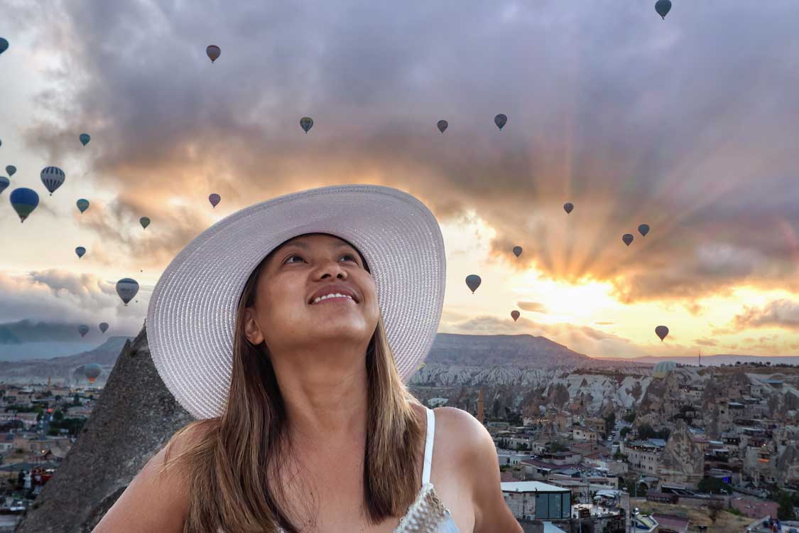 A woman standing below a sunrise sky filled with hot air balloons in Cappadocia, Turkiye one of the best places to go in Turkiye